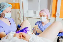 Concentrated woman gynecologist in mask with female assistant working with patient in operating room. Real transfer process or InVitro Fertilization and Embryo Transfer process.